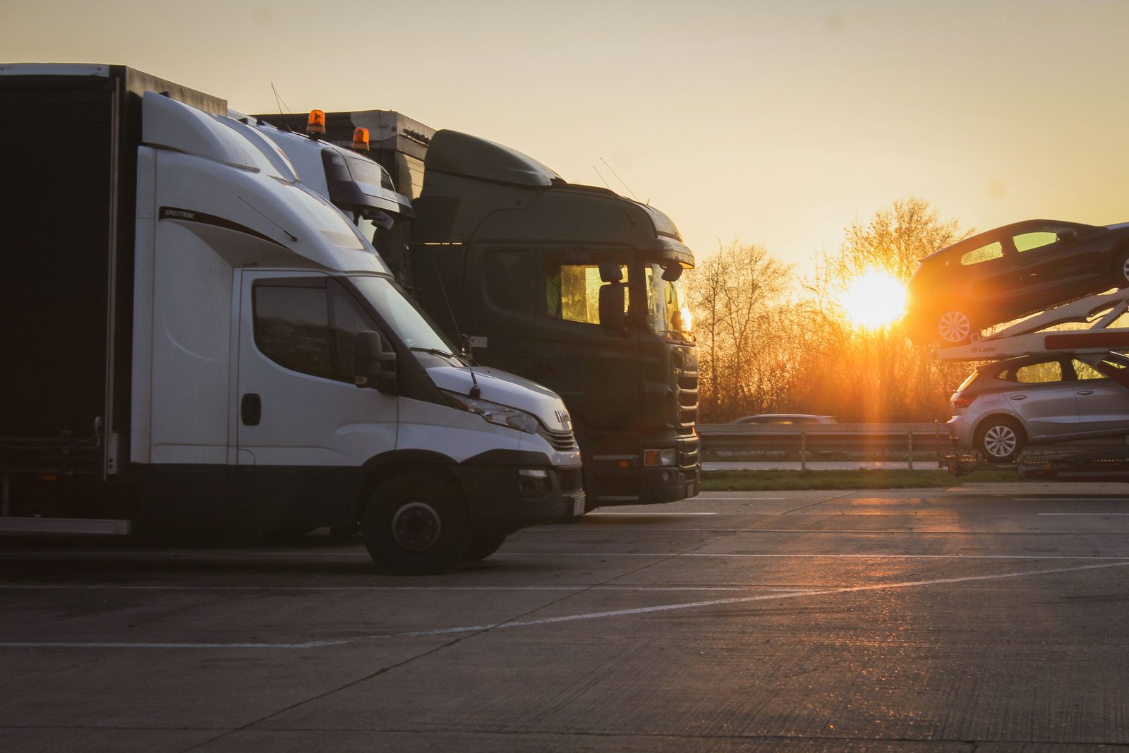 Vans, a truck cab and a car transporter parked at a highway stop at sunset